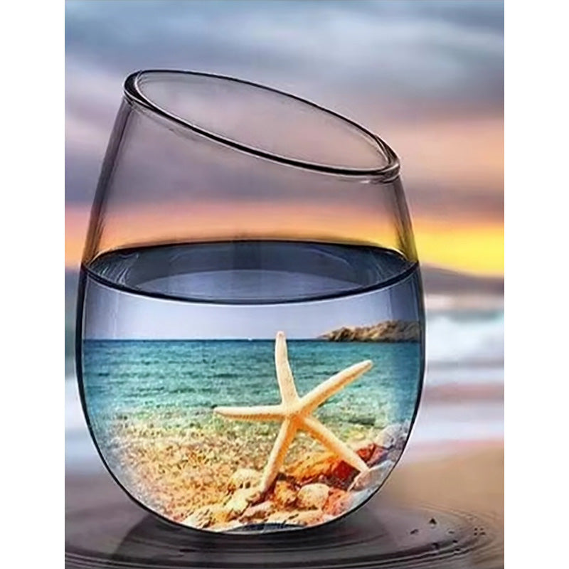 Glass with a starfish and beach scene inside, set against a blurred beach background.