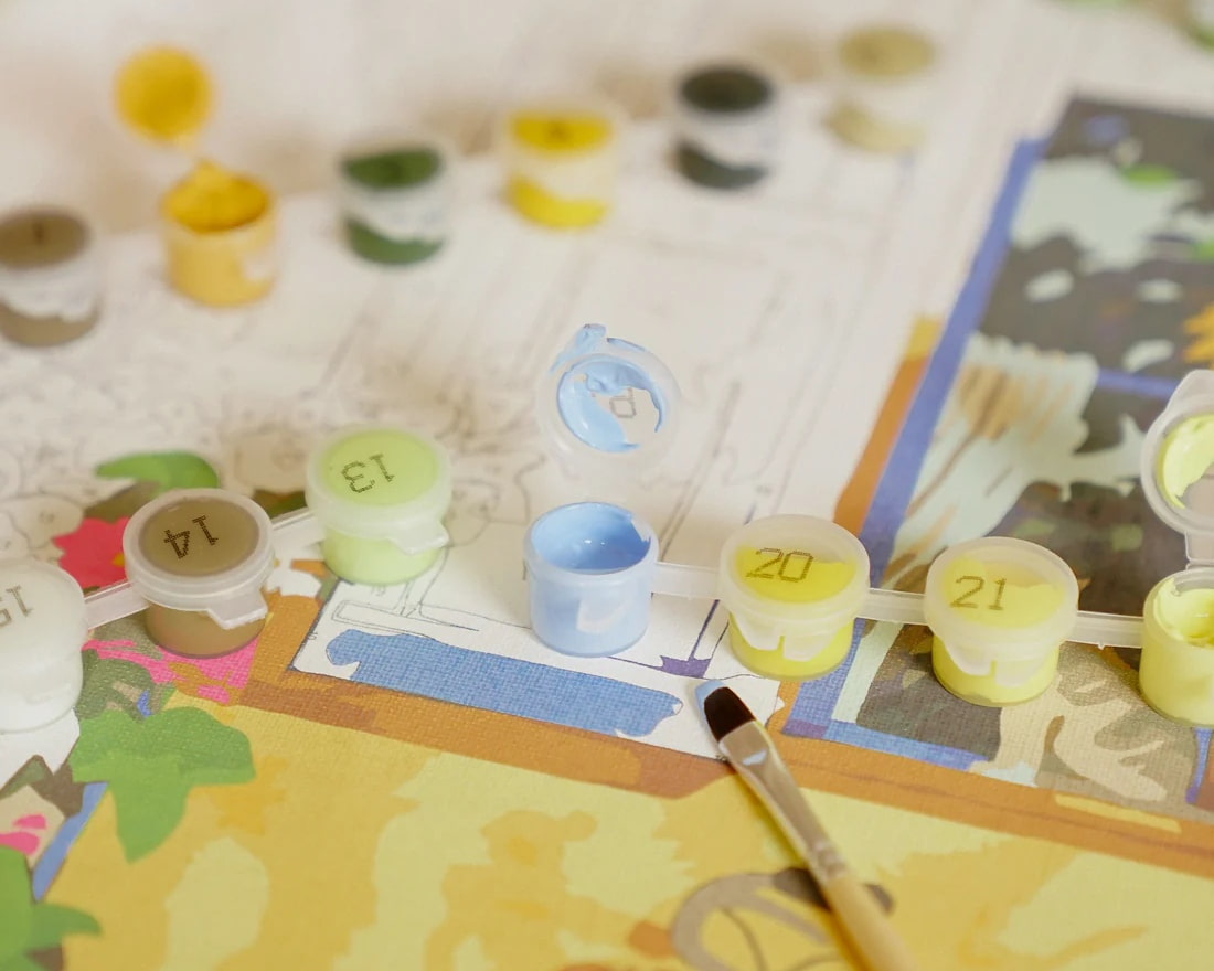 Paint-by-numbers kit setup with numbered paint pots and brush during a calm painting session