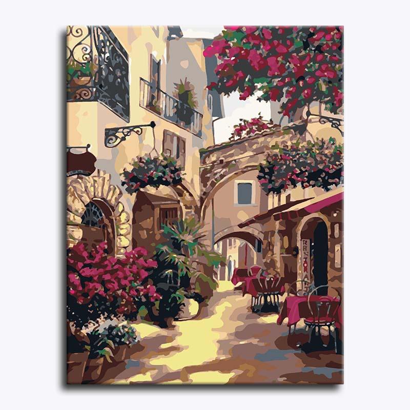 Painting of a picturesque street scene with flowers and tables.